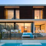 Fassade des Hauses LF115 in der Abenddämmerung mit Holzlamellen, Pool und beleuchteter Terrasse