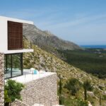 Seitenansicht des weißen Hauses am Hang mit Steinmauern und dem Meer im Hintergrund