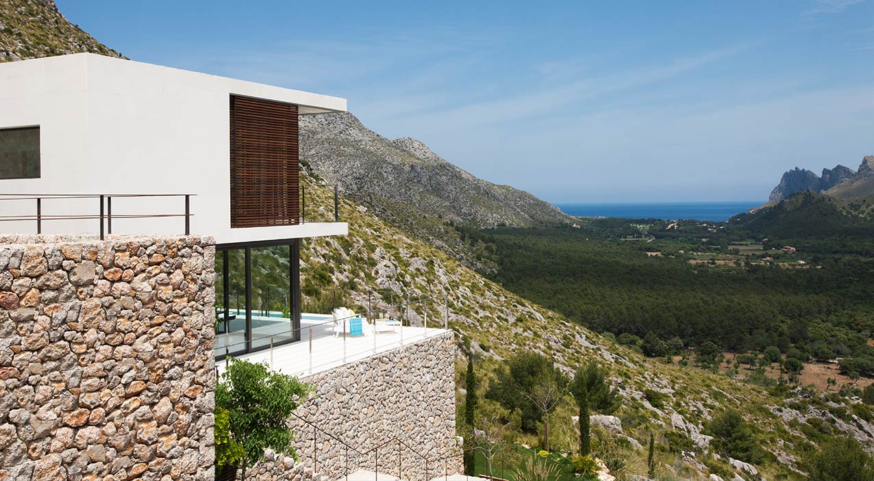 Seitenansicht des weißen Hauses am Hang mit Steinmauern und dem Meer im Hintergrund