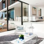 Zur Terrasse geöffnetes Wohnzimmer mit weißen Sofas, Couchtisch und Sonnenliegen auf Holzdeck