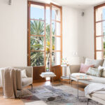 Salón del piso Antoni Maura con ventanales de madera, vistas a palmeras y sofá claro