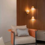 Butaca con respaldo trenzado naranja y cojines beige, panel de madera y tres apliques dorados encendidos