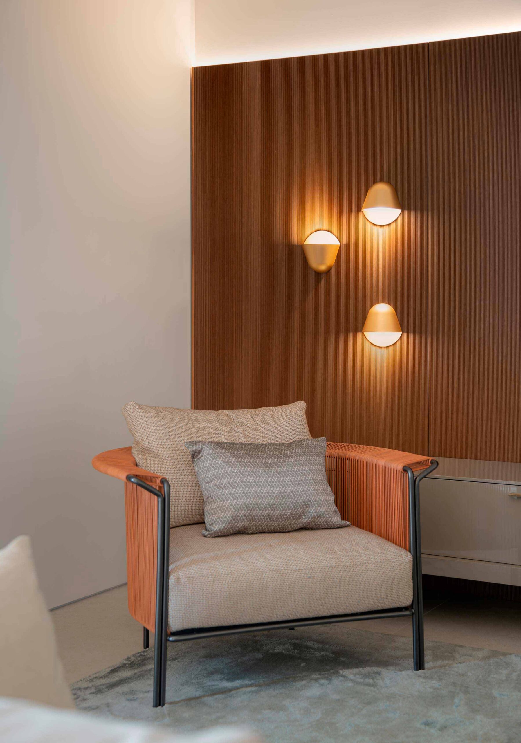 Butaca con respaldo trenzado naranja y cojines beige, panel de madera y tres apliques dorados encendidos