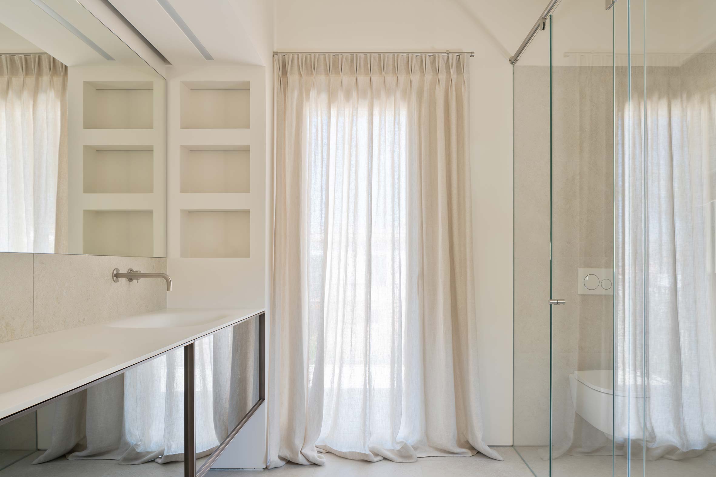 Baño con lavabo doble blanco, espejo, nichos empotrados, cortina translúcida y mampara de cristal