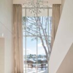Hall de doble altura con lámpara geométrica, gran ventanal y vistas a la bahía con barcas