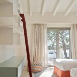Dormitorio con dos camas de faldón naranja, estantería con escalera roja y vistas a la bahía