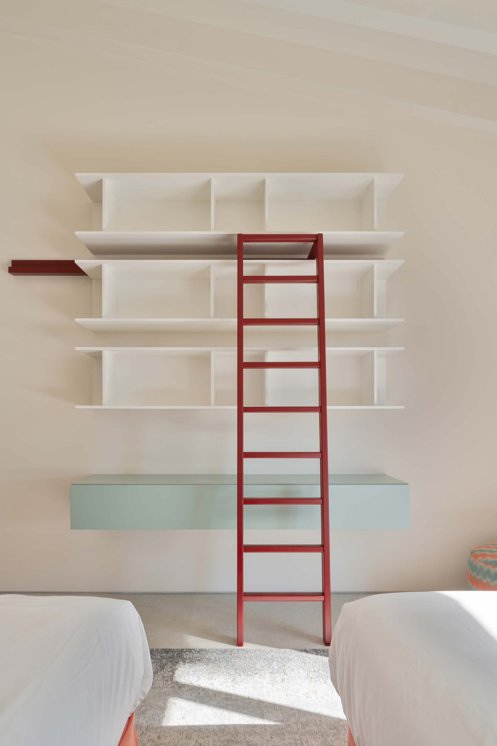 Estantería blanca con escalera roja y mueble suspendido verde agua entre dos camas