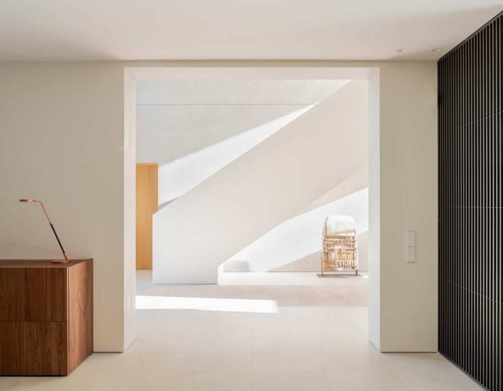 Vestíbulo con escalera blanca escultórica, aparador de madera oscura y panel de lamas negras