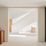 Vestíbulo con escalera blanca escultórica, aparador de madera oscura y panel de lamas negras