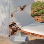 Tumbona de madera con cojín blanco y tela de lino, mesa auxiliar gris y suelo de terraza