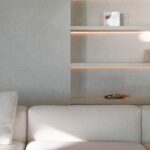 Detalle del salón con sofá crema y estantes empotrados con luz indirecta sobre pared en tono piedra