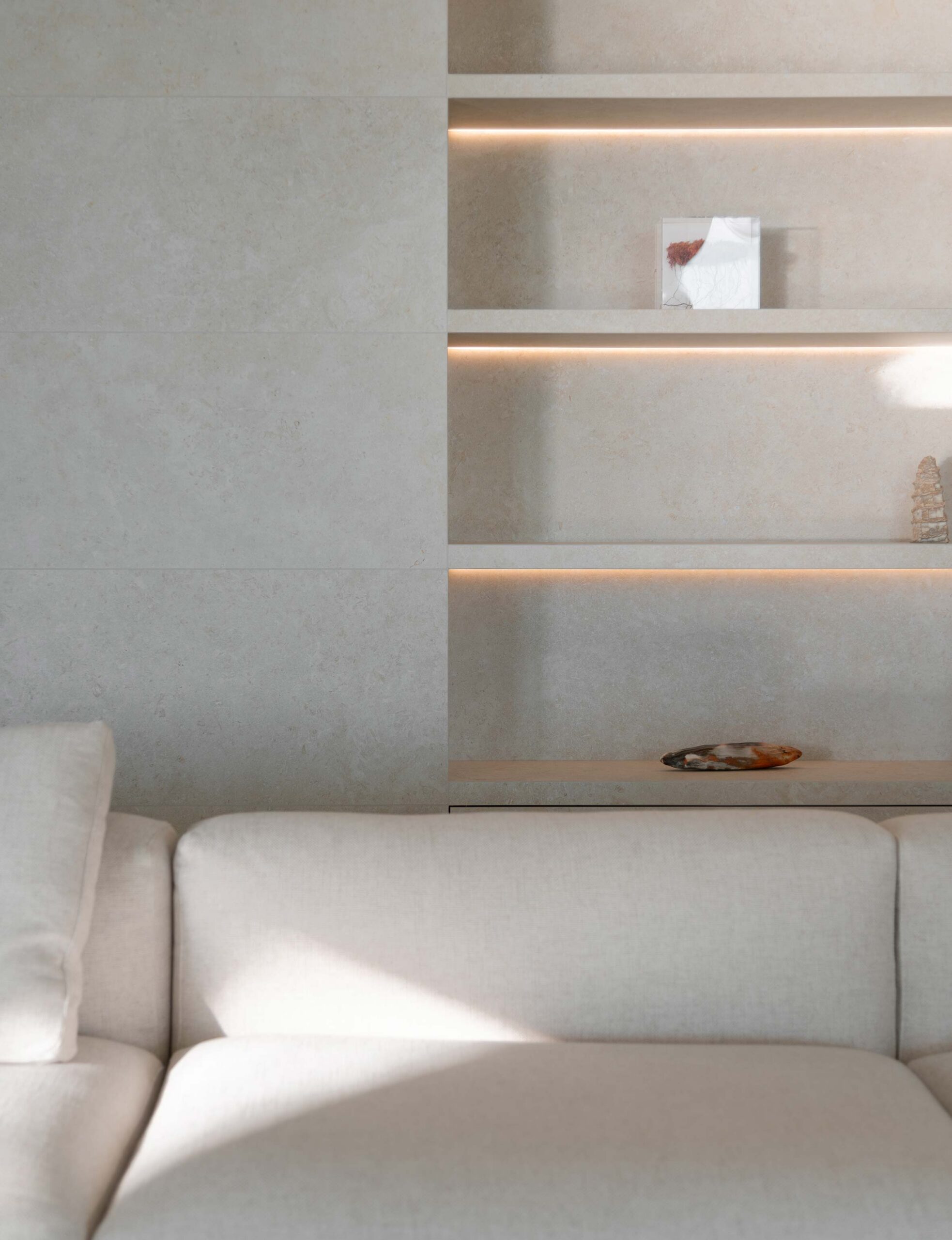 Detalle del salón con sofá crema y estantes empotrados con luz indirecta sobre pared en tono piedra