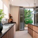 Cocina con encimera oscura, muebles de madera, fregadero y puerta acristalada abierta al jardín