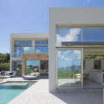 Terraza de pavimento claro junto a la piscina, con cocina abierta al exterior y ladera verde