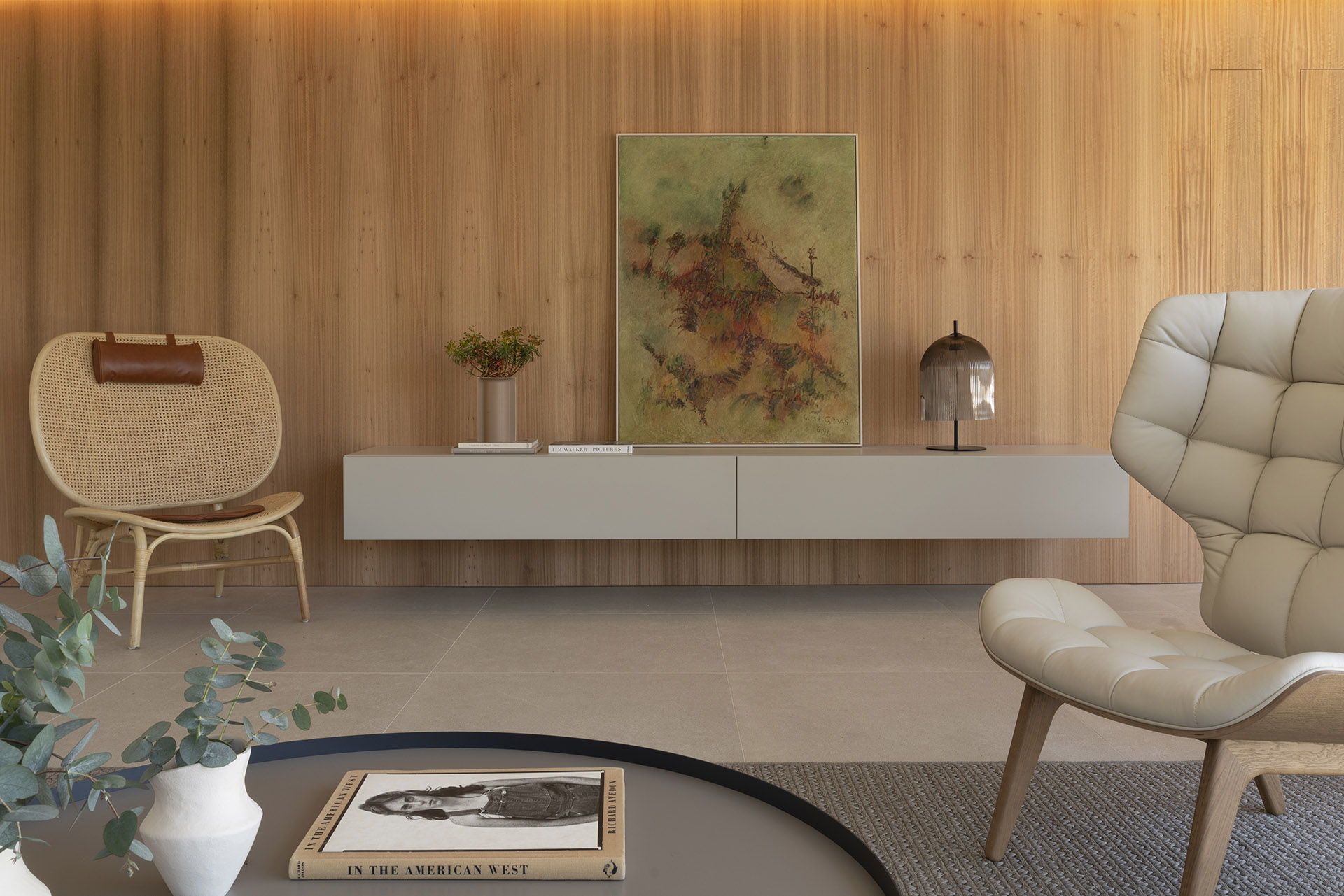 Salón con pared de madera clara, aparador flotante gris, cuadro abstracto, sillón de ratán y butaca beige