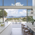 Cocina con isla de encimera de piedra veteada, mesa de comedor y terraza con vistas al mar