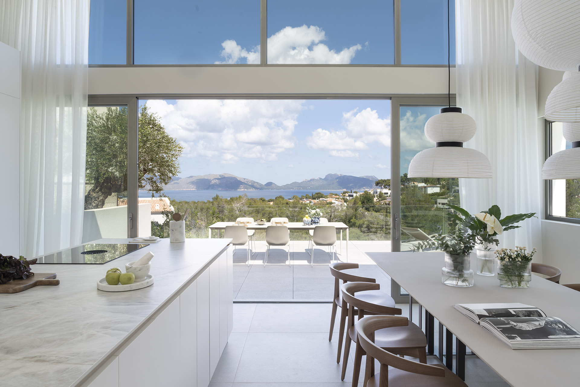 Cocina con isla de encimera de piedra veteada, mesa de comedor y terraza con vistas al mar