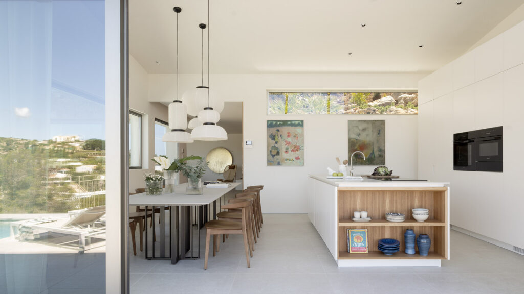 Cocina con isla blanca y estantería de madera, lámparas colgantes de papel y mesa de comedor