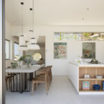 Cocina con isla blanca y estantería de madera, lámparas colgantes de papel y mesa de comedor
