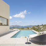 Terraza con piscina, tumbona curva y muro beige, con vistas al mar y a las montañas