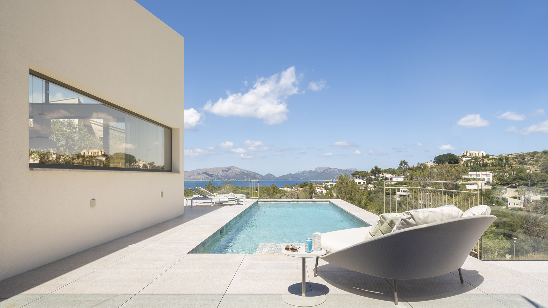 Terraza con piscina, tumbona curva y muro beige, con vistas al mar y a las montañas