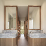 Baño con dos lavabos de mármol gris sobre muebles de madera, espejos enmarcados y vestidor al fondo