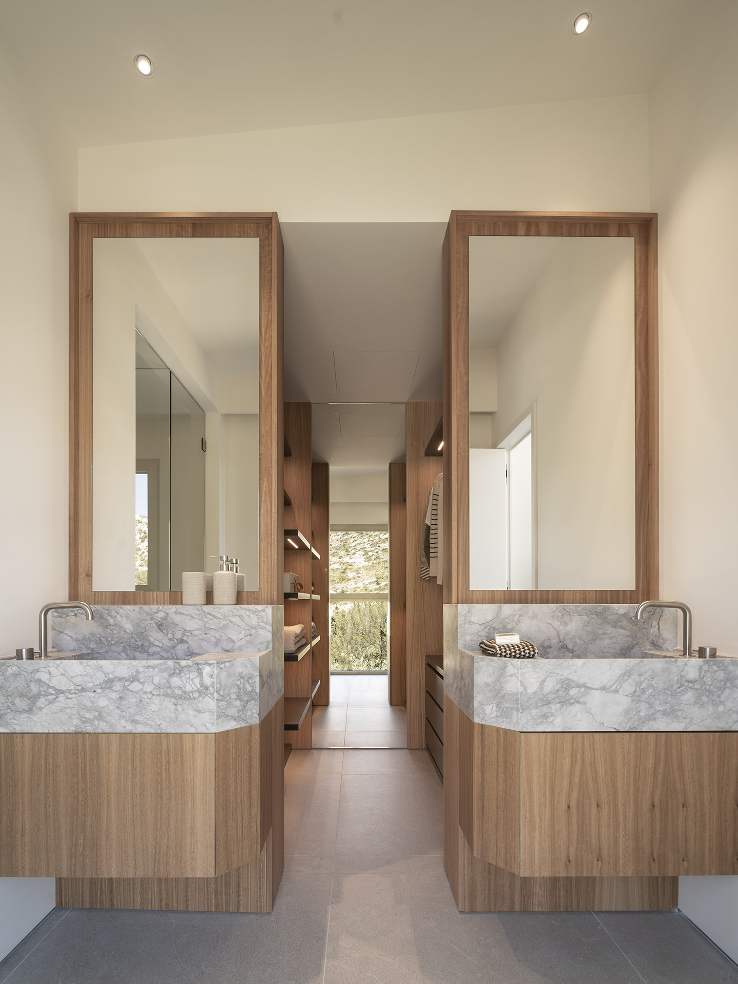 Baño con dos lavabos de mármol gris sobre muebles de madera, espejos enmarcados y vestidor al fondo