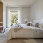 Dormitorio con cama doble, escritorio integrado en madera, alfombra geométrica y ventanal al jardín
