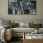 Beige sofa with green cushions beneath an abstract painting and a timber coffee table