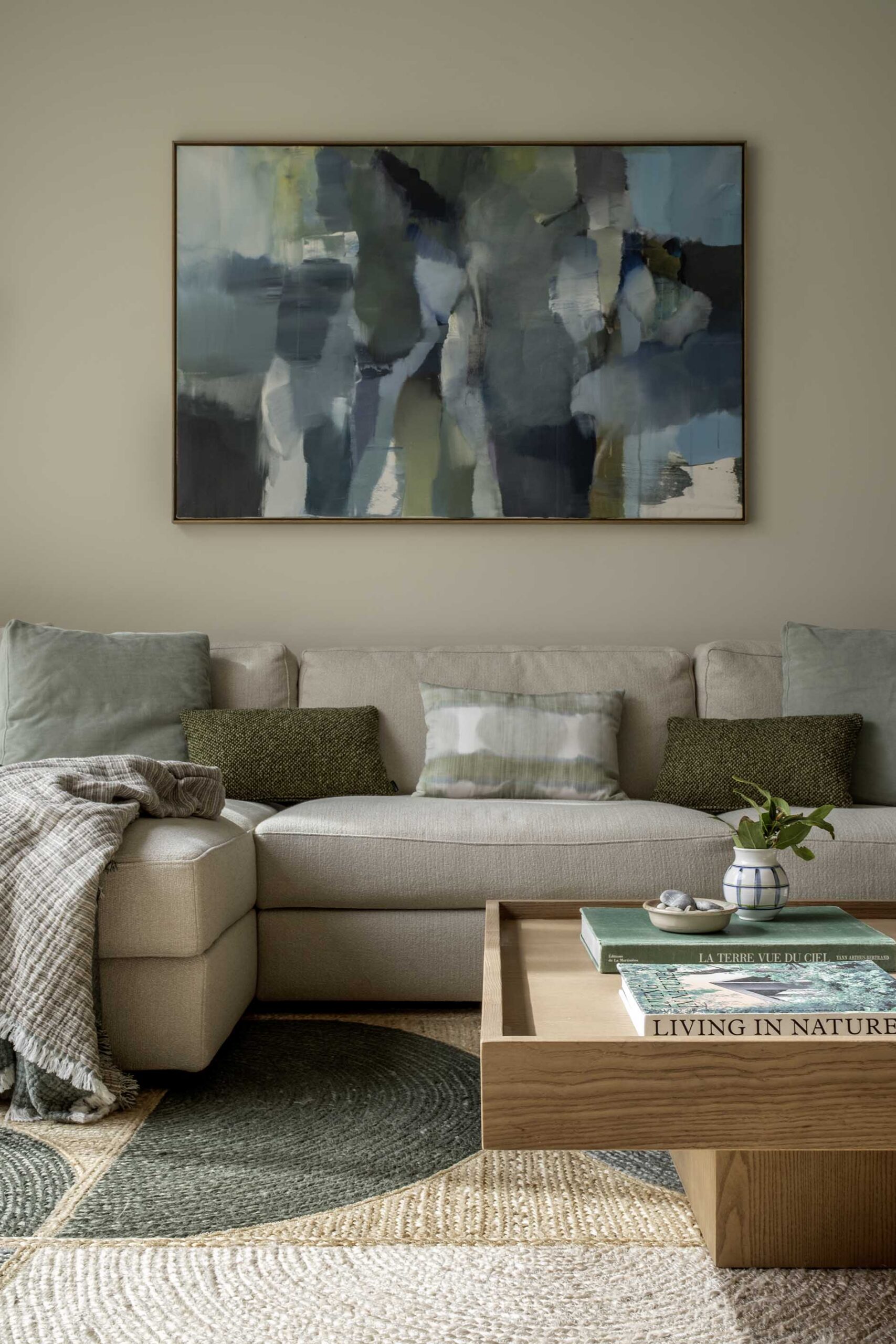 Beige sofa with green cushions beneath an abstract painting and a timber coffee table