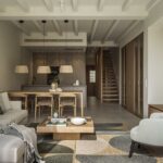 Open-plan living area with sofa, dining area, kitchen at the back, wooden staircase and stone wall