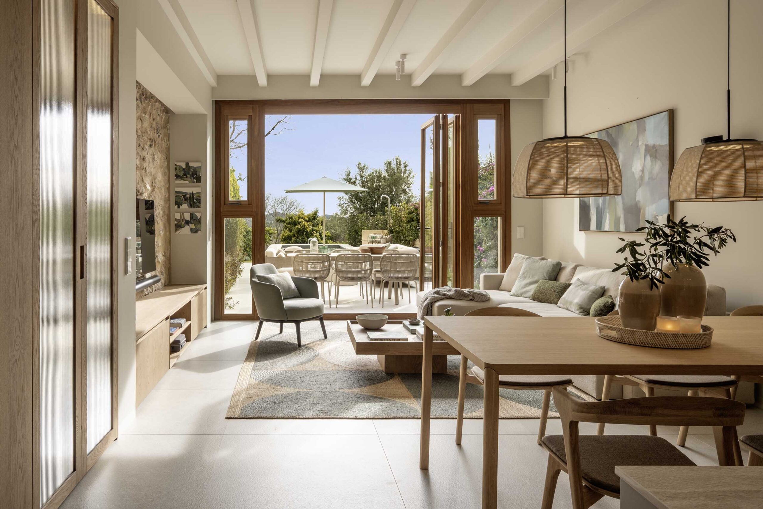 Bright living and dining room with wicker lamps, wooden table and doors open onto the terrace
