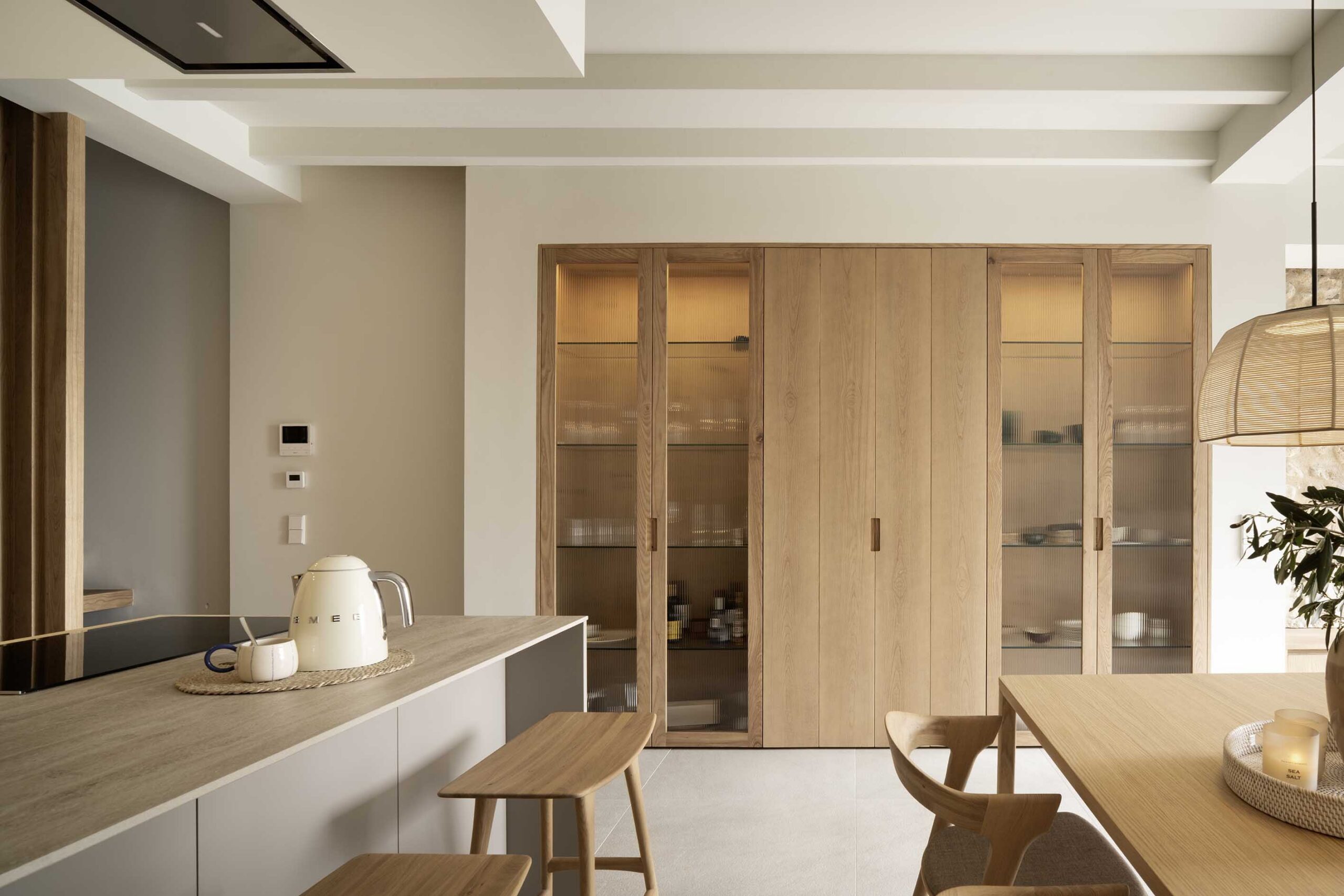 Open kitchen with island, wooden stools and wooden cabinet with fluted glass doors