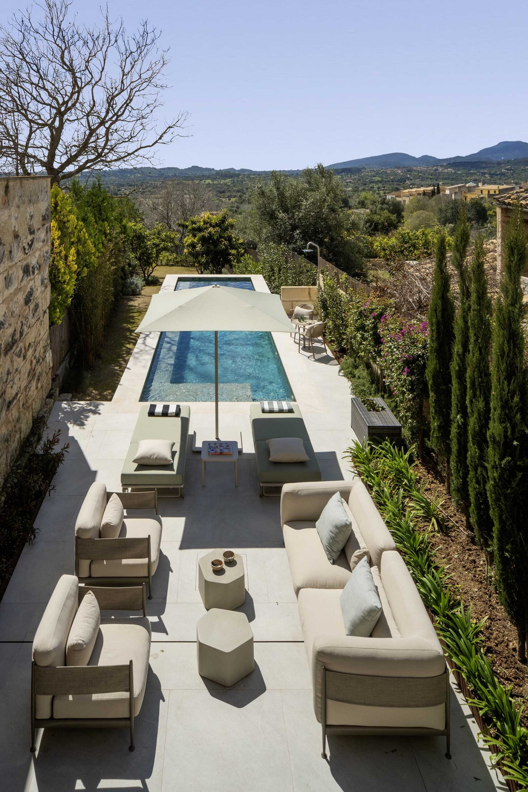 Aerial view of the terrace with pool, sun loungers, sofas, cypress trees and mountains in the background