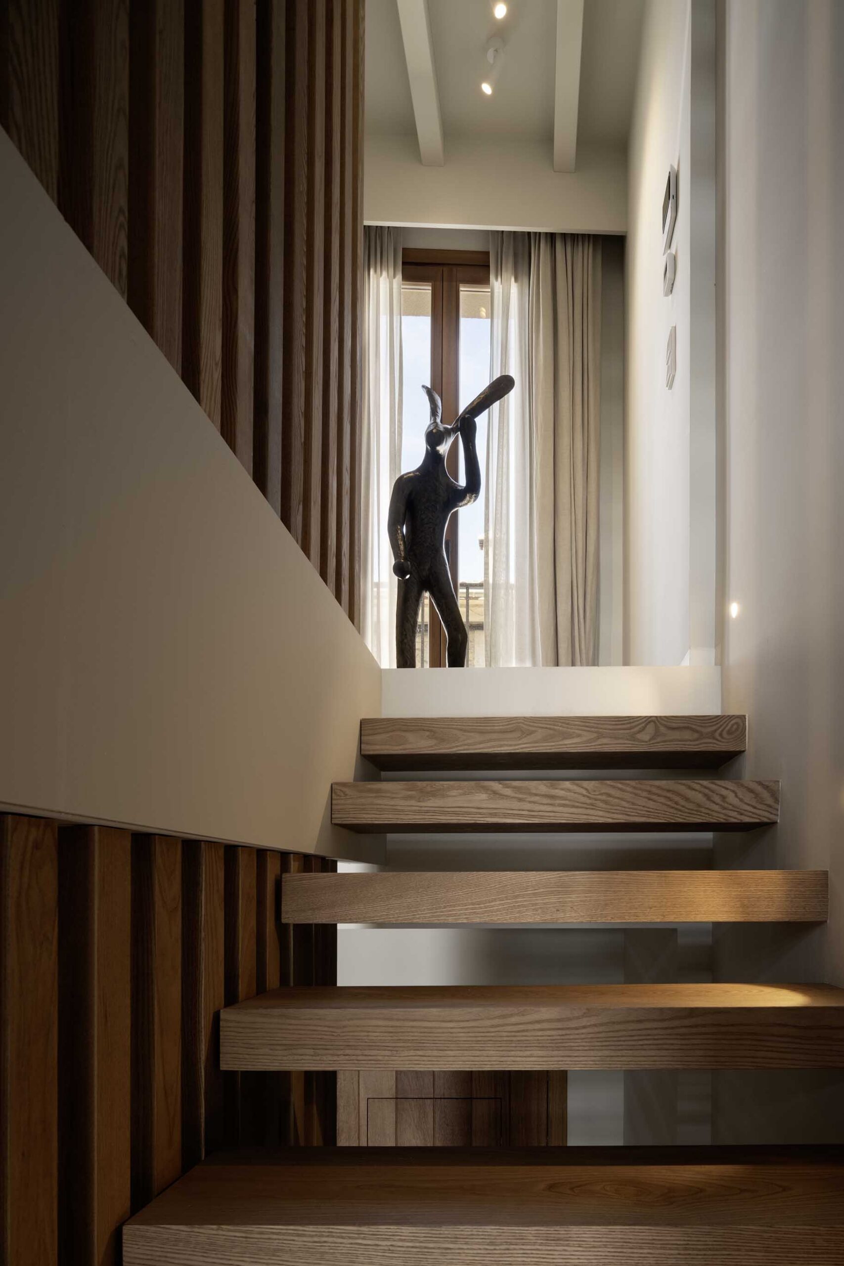 Staircase with timber treads and vertical slats, and a dark sculpture in the background