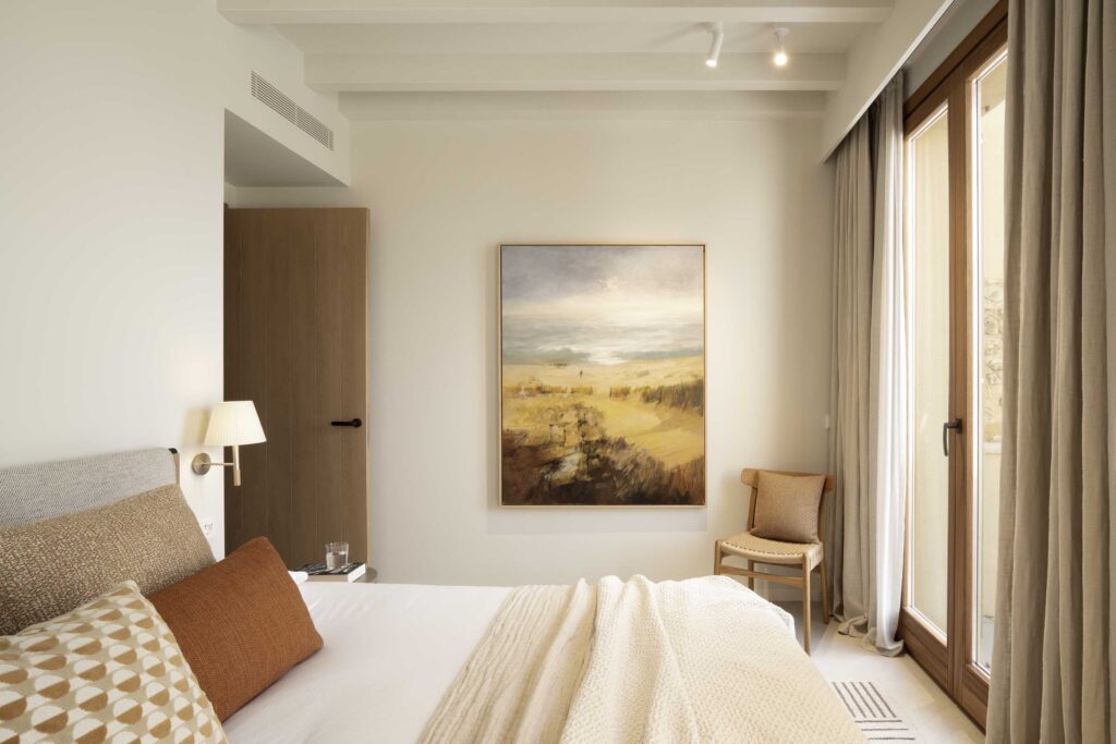 Bedroom with landscape painting, sand-coloured curtains, wooden door and large window with natural light