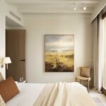 Bedroom with landscape painting, sand-coloured curtains, wooden door and large window with natural light