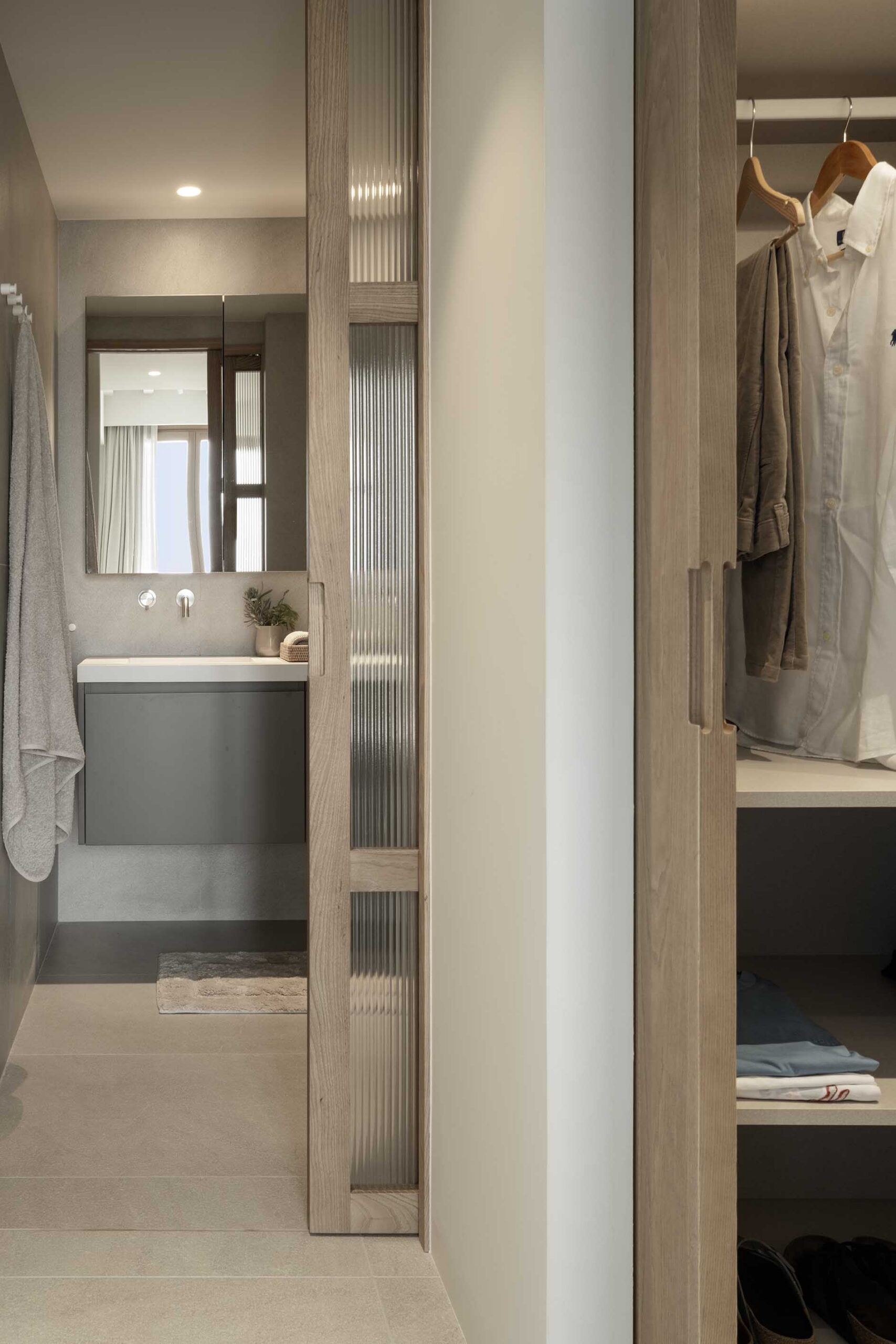 Sliding fluted glass door to the bathroom and open wardrobe with hanging clothes
