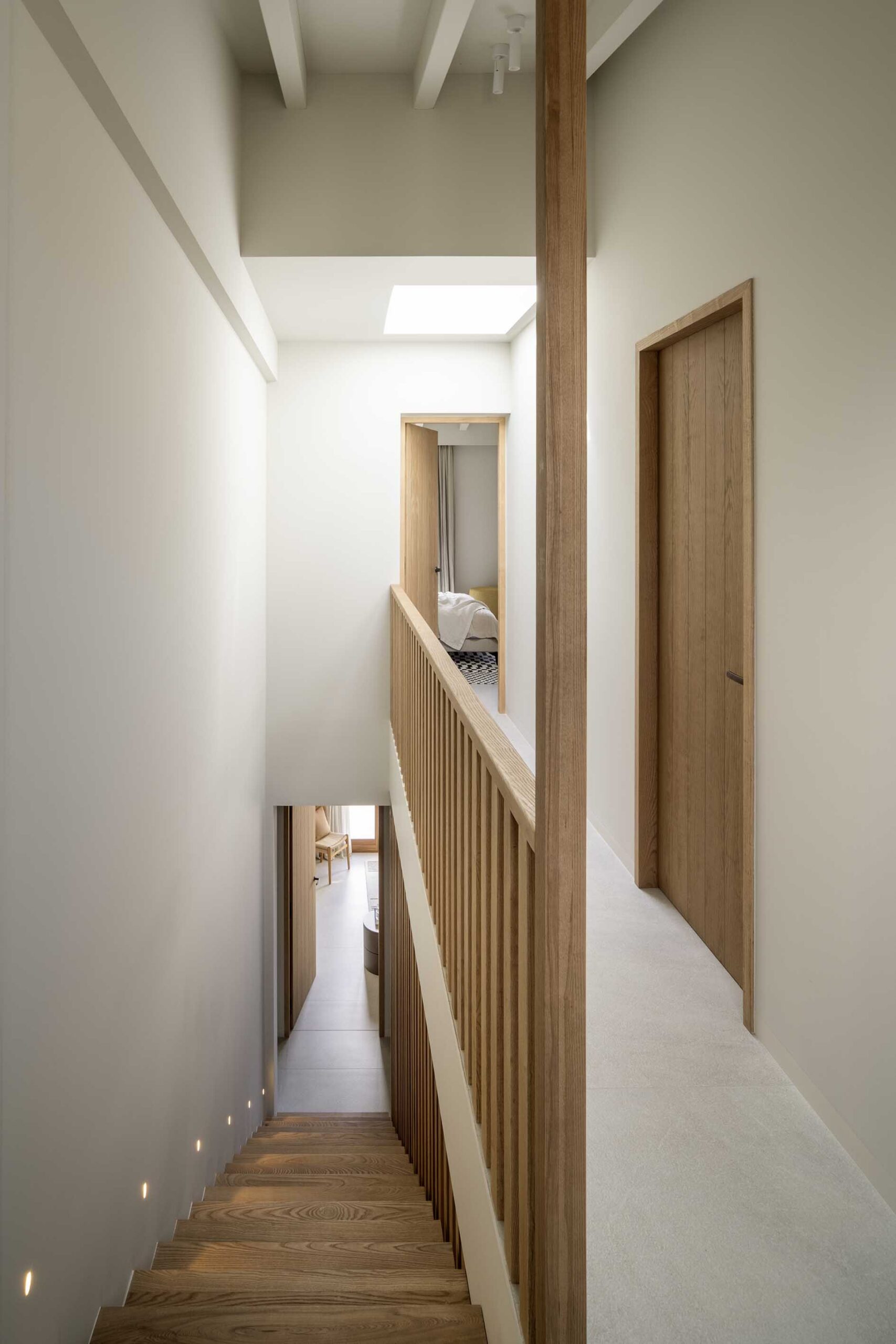 Corridor with wooden staircase, balustrade of vertical slats, wooden doors and rooflight