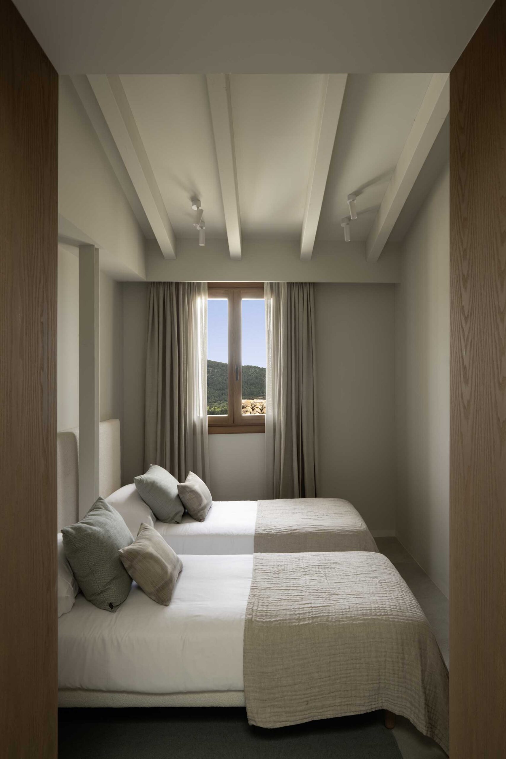 Bedroom with two beds, green cushions, white-beamed ceiling and mountain views