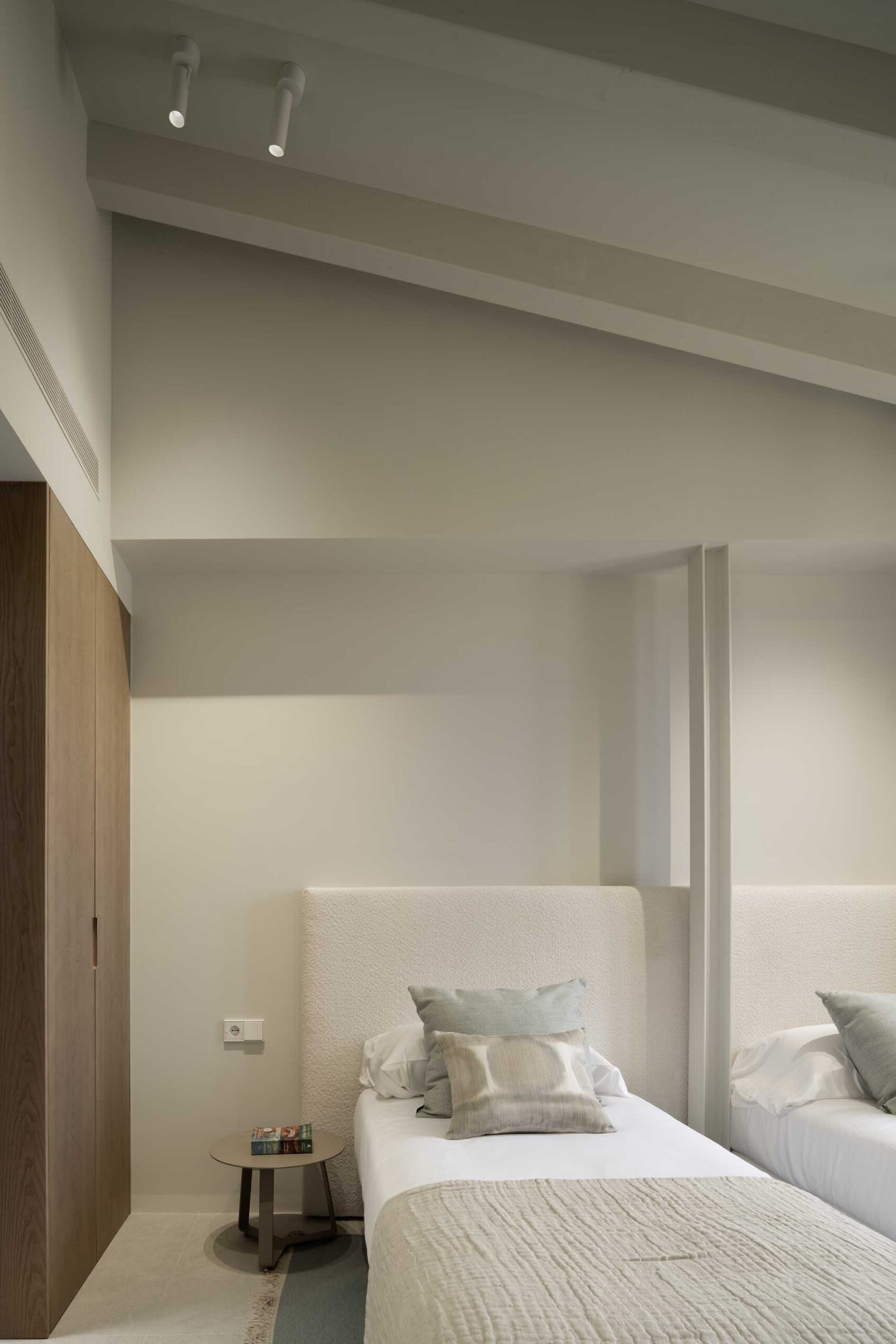Bedroom detail with two beds, light upholstered headboards, wooden wardrobe and ceiling spotlights