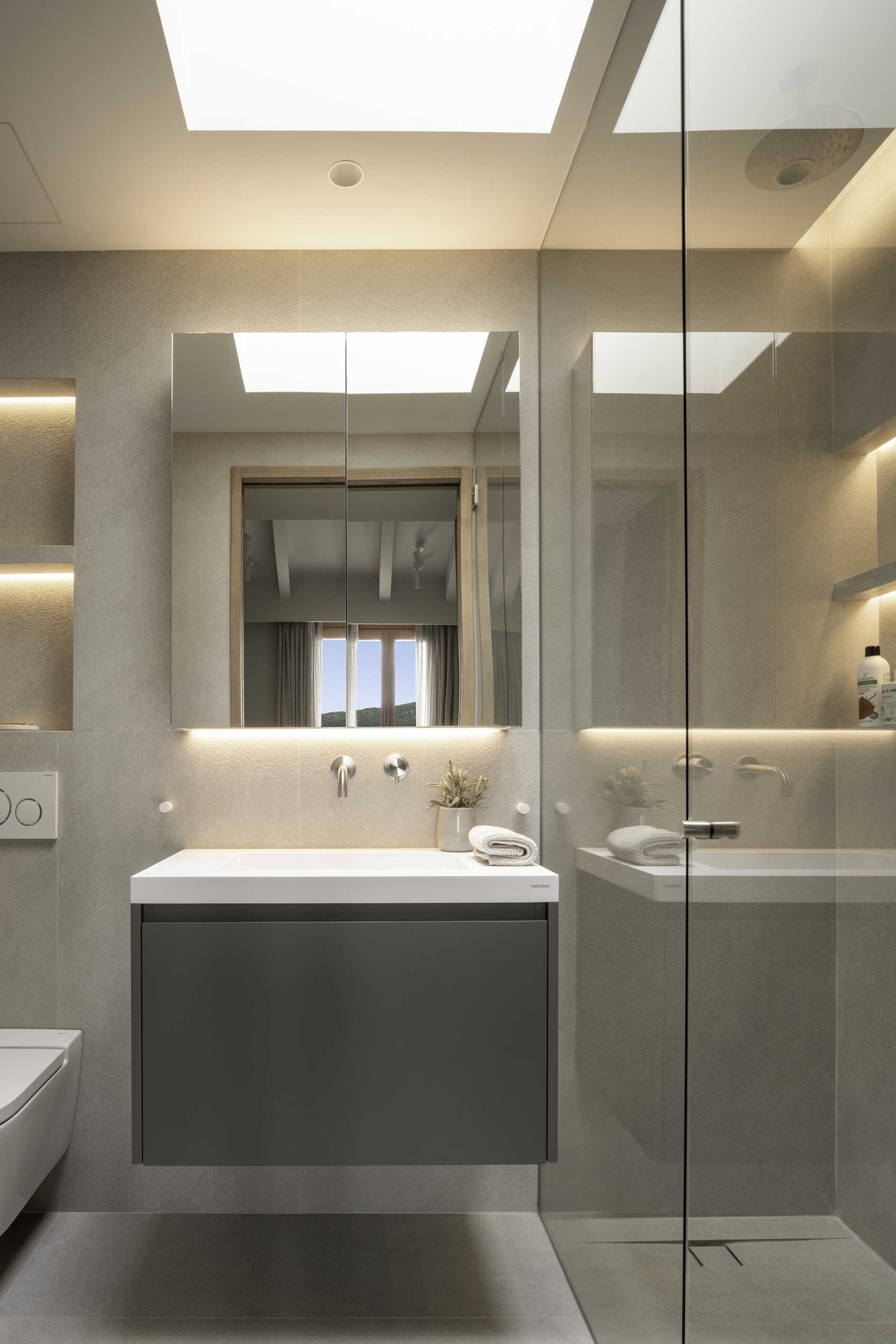 Bathroom with wall-hung greyish-green basin, illuminated mirror, glass shower and rooflight in the ceiling