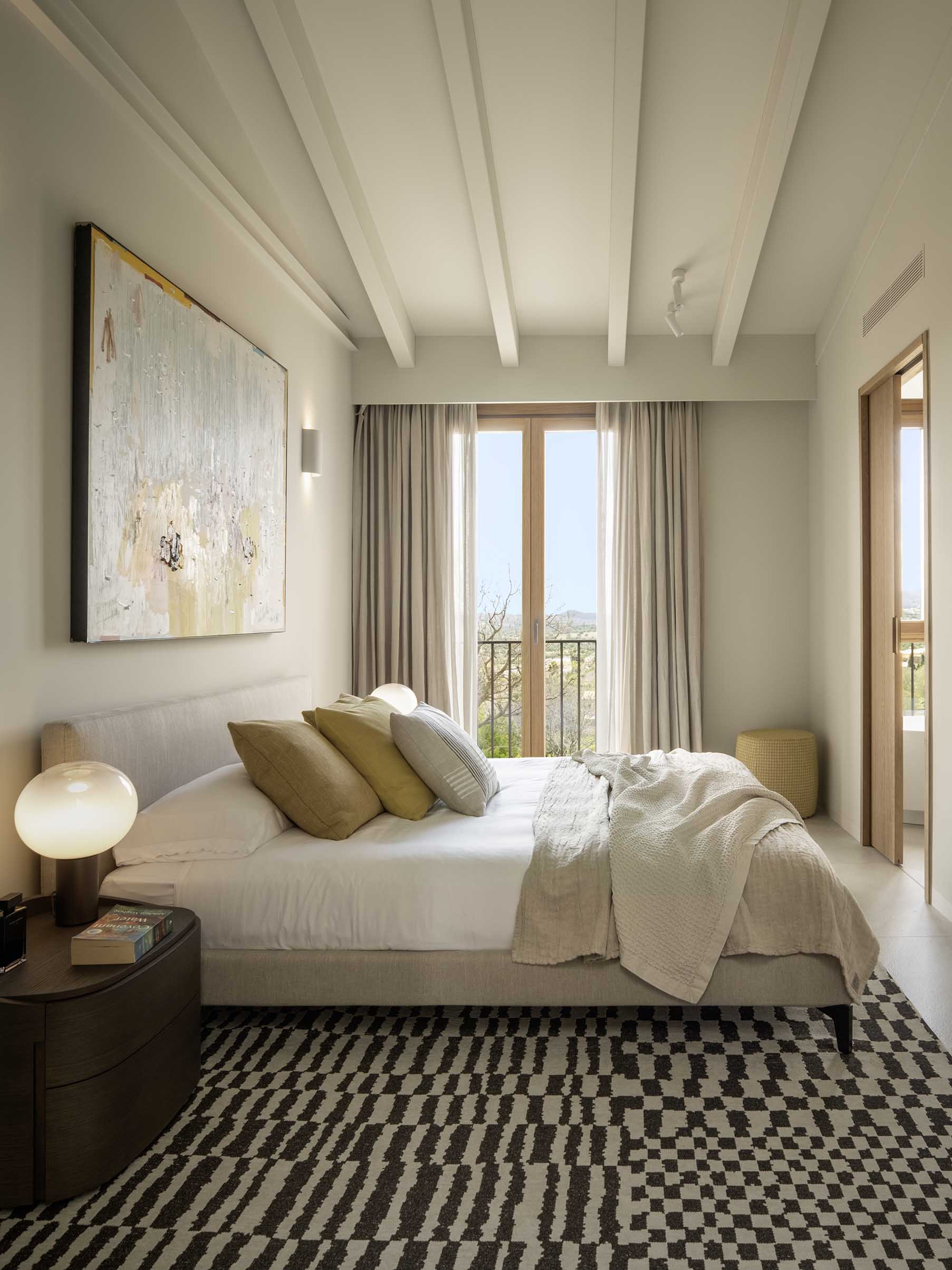 General view of the bedroom with white beams, black and white geometric rug and balcony