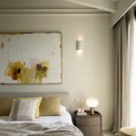 Bedroom with yellow-accented abstract painting, mustard cushions, bedside table with lamp and chequerboard rug