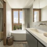Bathroom with freestanding bath beside a timber window, white double basin and views of the landscape