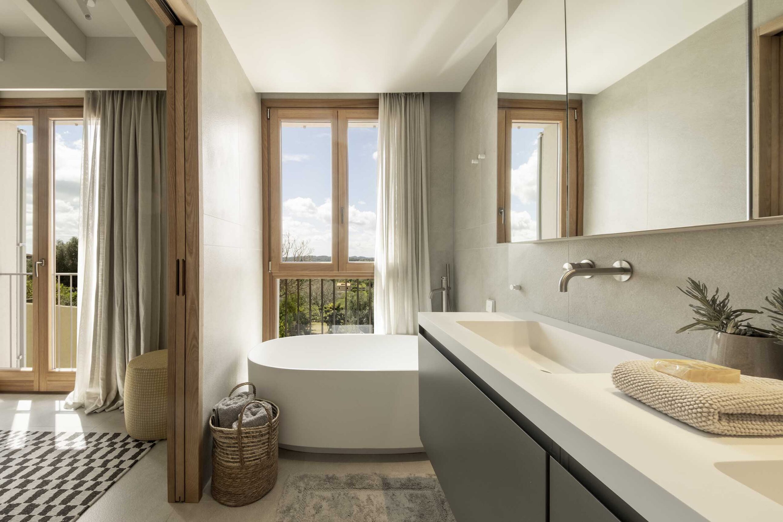 Bathroom with freestanding bath beside a timber window, white double basin and views of the landscape