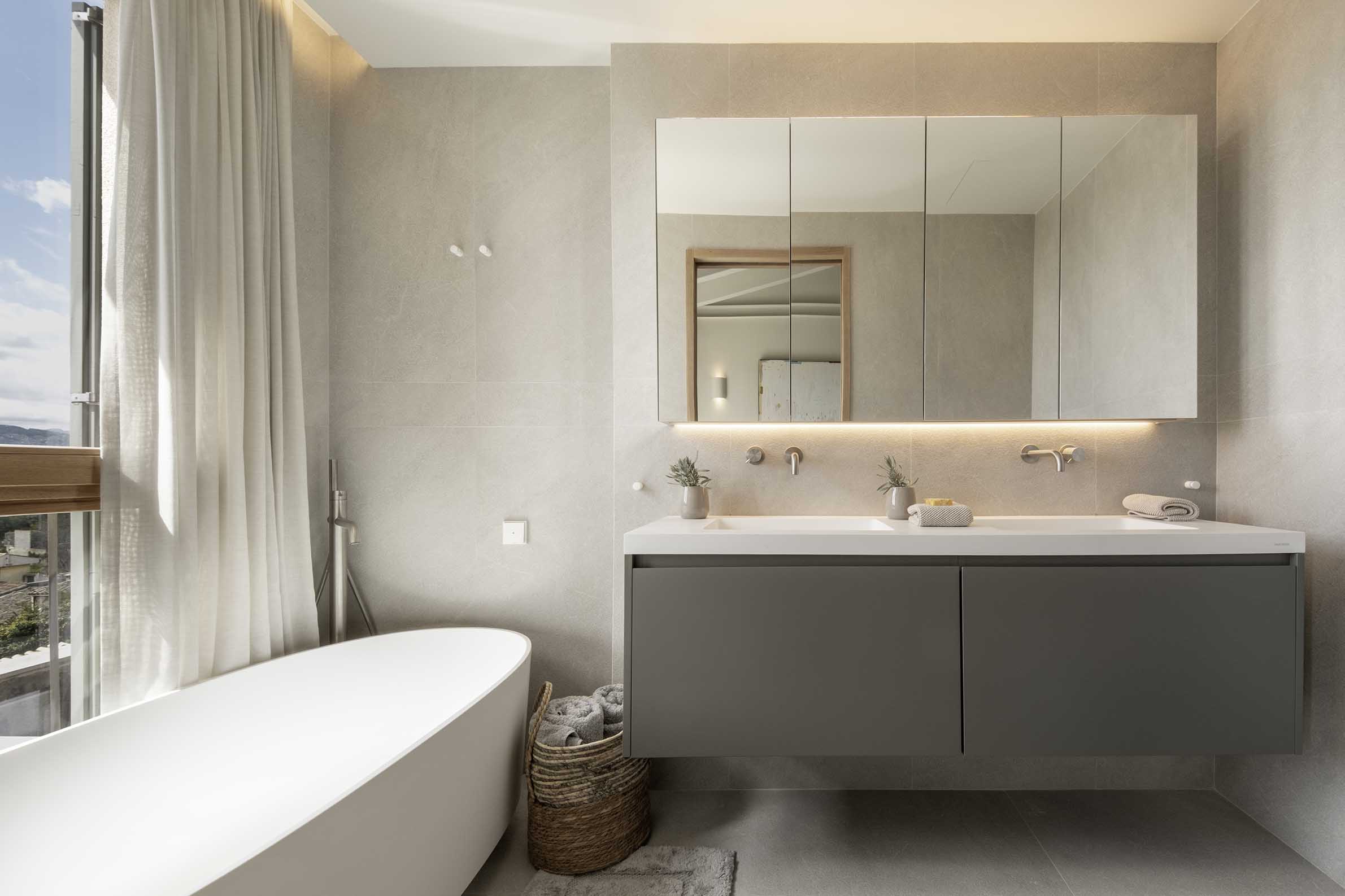 Bathroom with white freestanding bath, grey wall-hung double basin and mirrors with indirect lighting