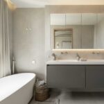 Bathroom with sandy grey walls, freestanding bath, large window with sheer curtains and wall-hung vanity unit