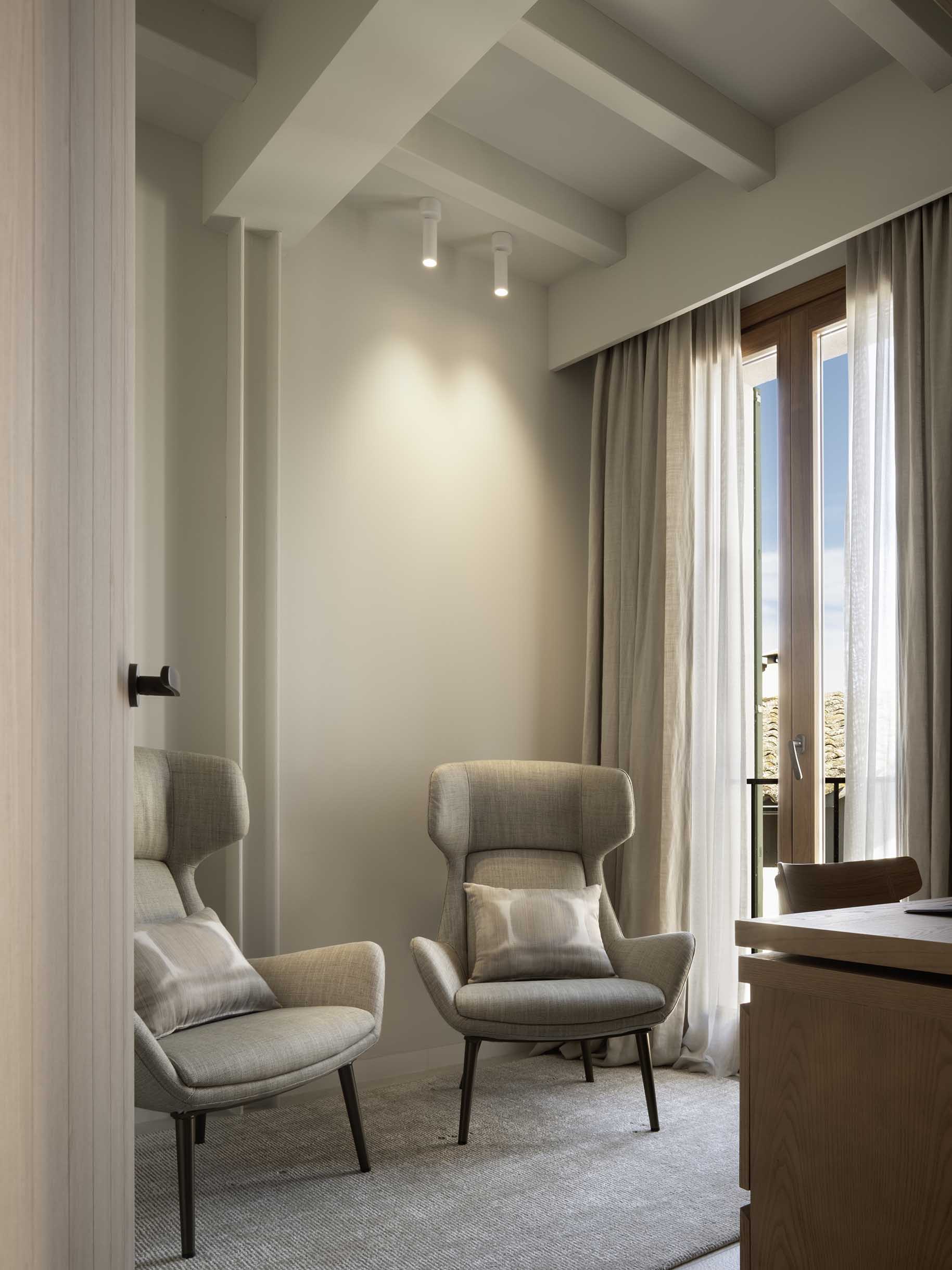 Study with two upholstered wing armchairs, wooden desk and French window with curtains