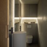 Guest WC with white cylindrical basin, grey cladding and integrated indirect lighting